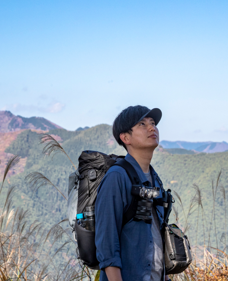 メインビジュアルすすきが生えた山頂で青空を見上げるJINさん