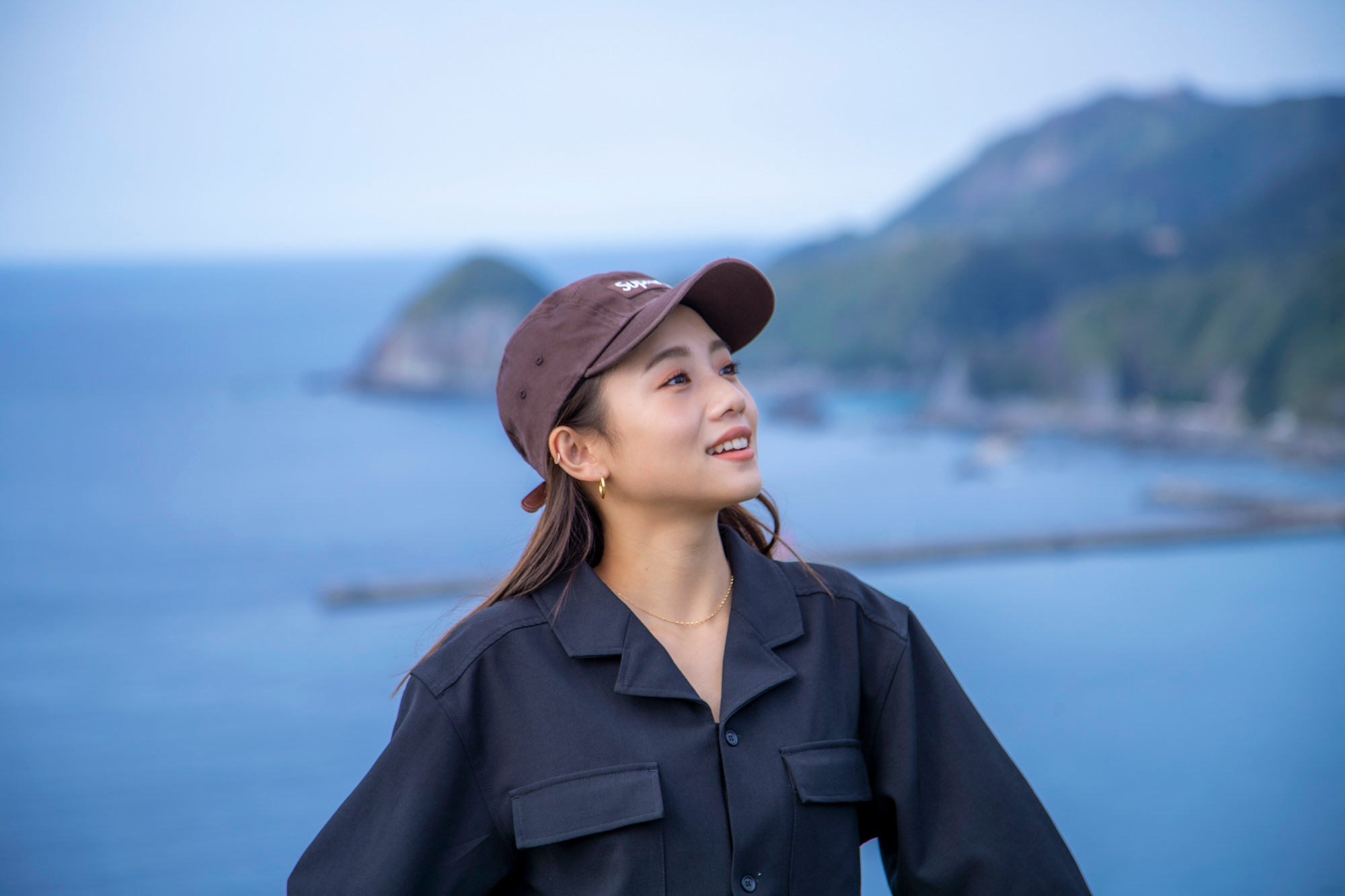高台で海と港の風景をバックに絶景を楽しむアオイさん