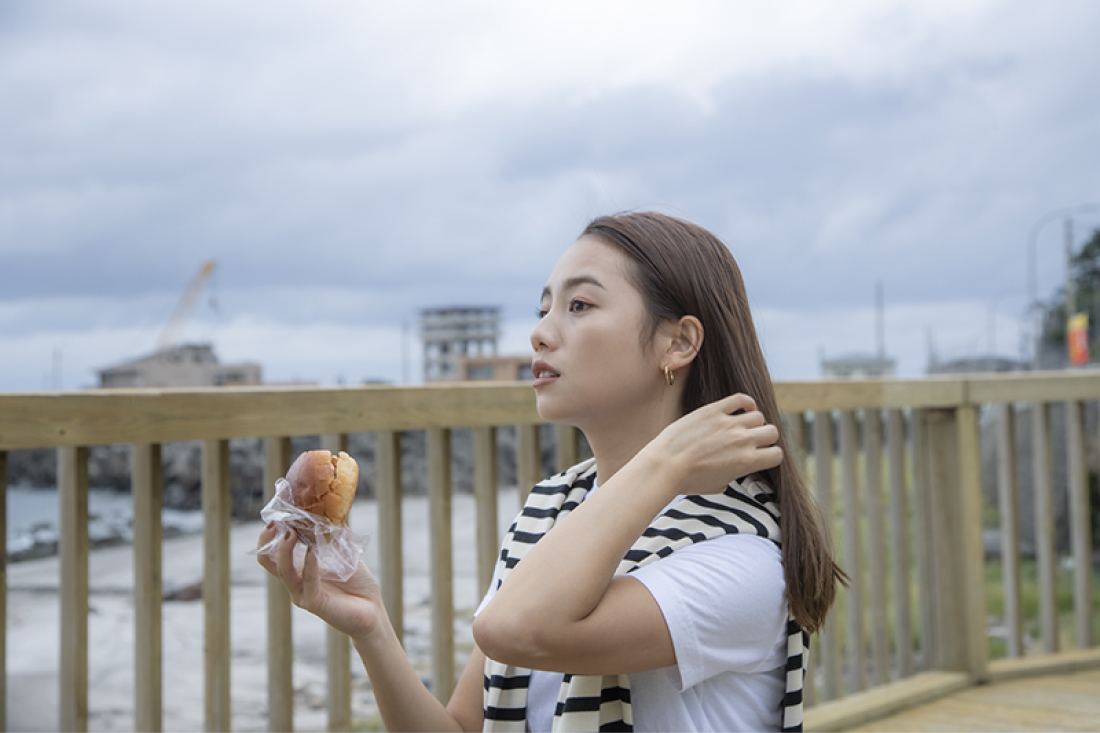 海辺で気持ちいい風にあたり、海を眺めながらパンを食べるアオイさん