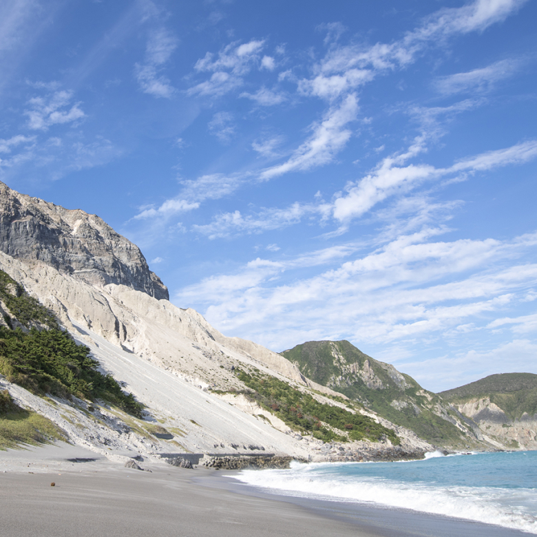 天上山のむき出しの山肌と、白い砂浜と海の風景