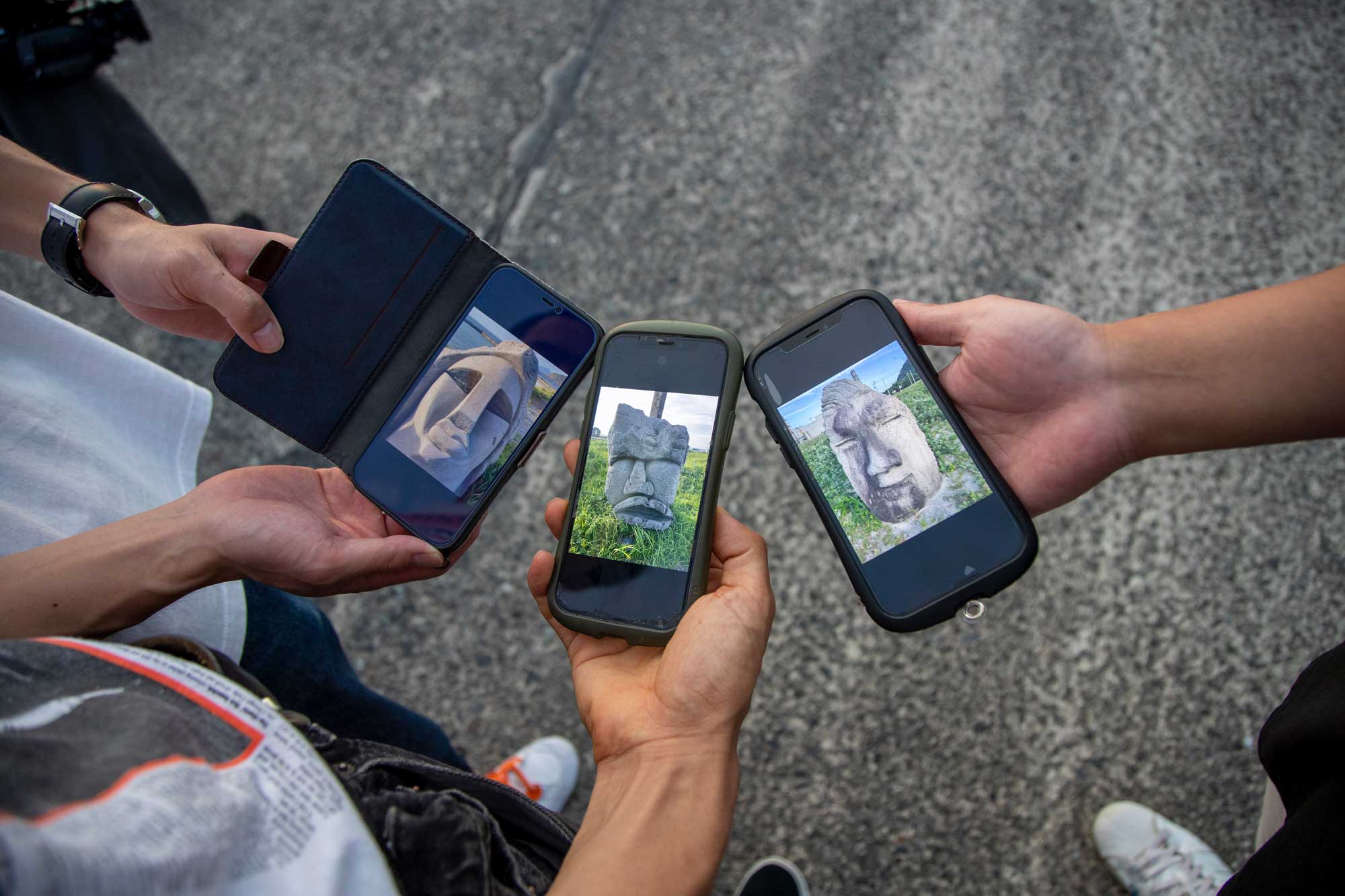 3人それぞれが自分に似たモヤイ像をスマホで撮影して見せ合っている
