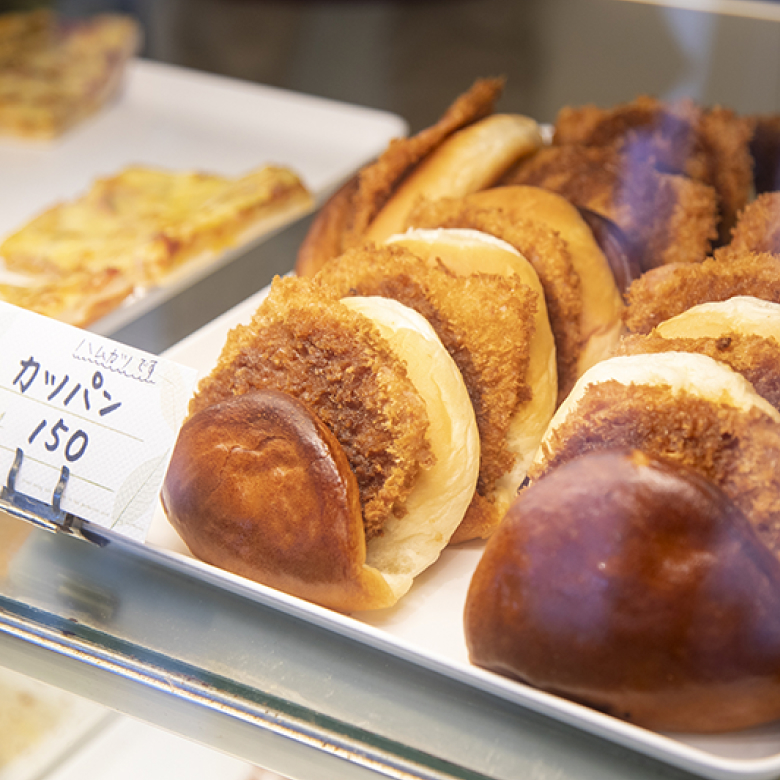 お店に並んだパン。値札に「カツパン150円（ハムカツです）」と書かれてる。
