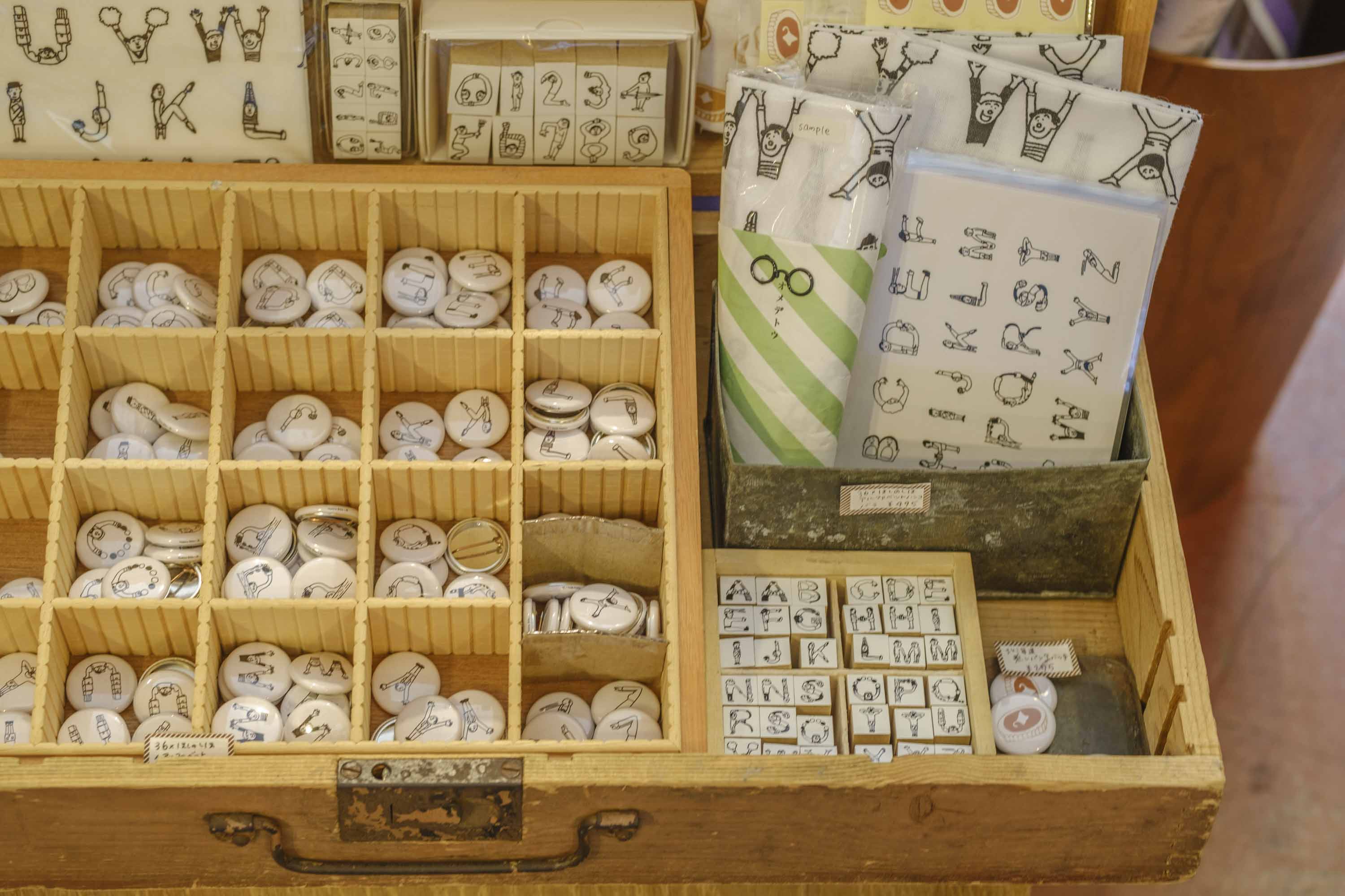 「人アルファベットシリーズ」缶バッチ275円など
