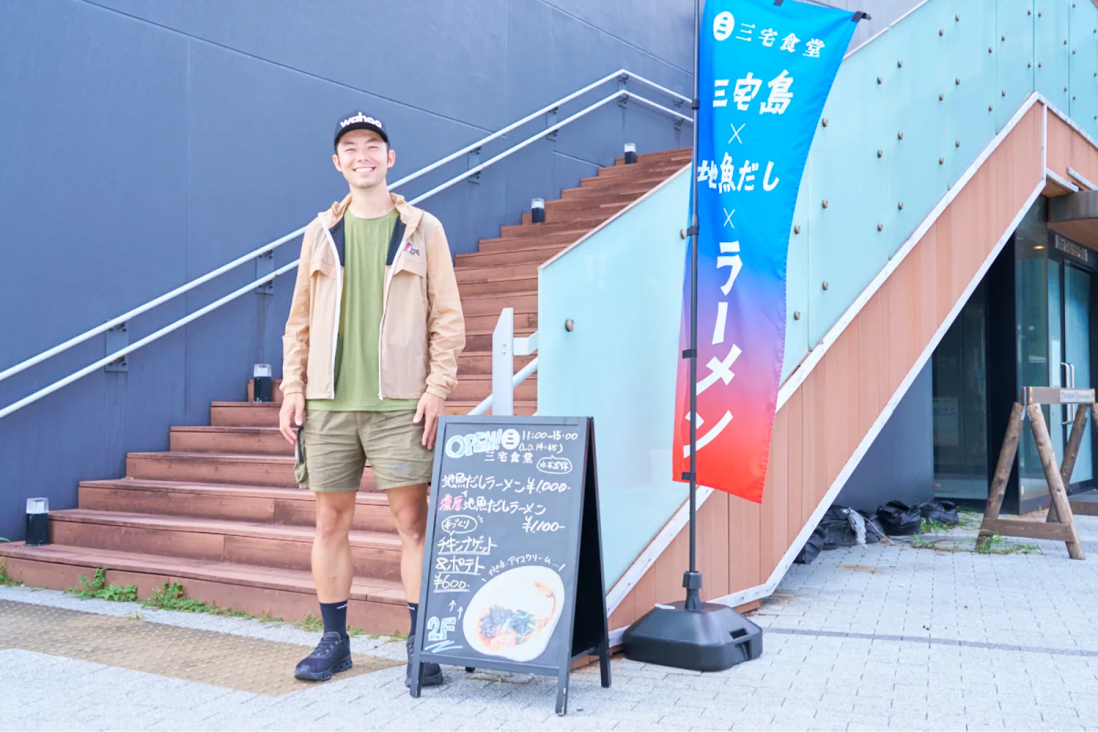 三宅食堂の看板の前で笑顔を見せるけんたさん