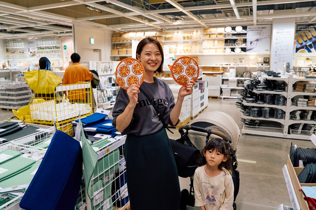 オレンジ柄のキッチン用品を両手に持って満面の笑みを浮かべるママ