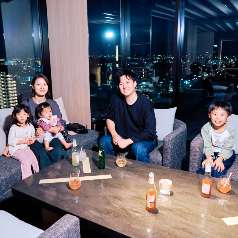 ソラノホテルからの夜景を背に、ソファに座ってドリンクを楽しむおりおりん一家