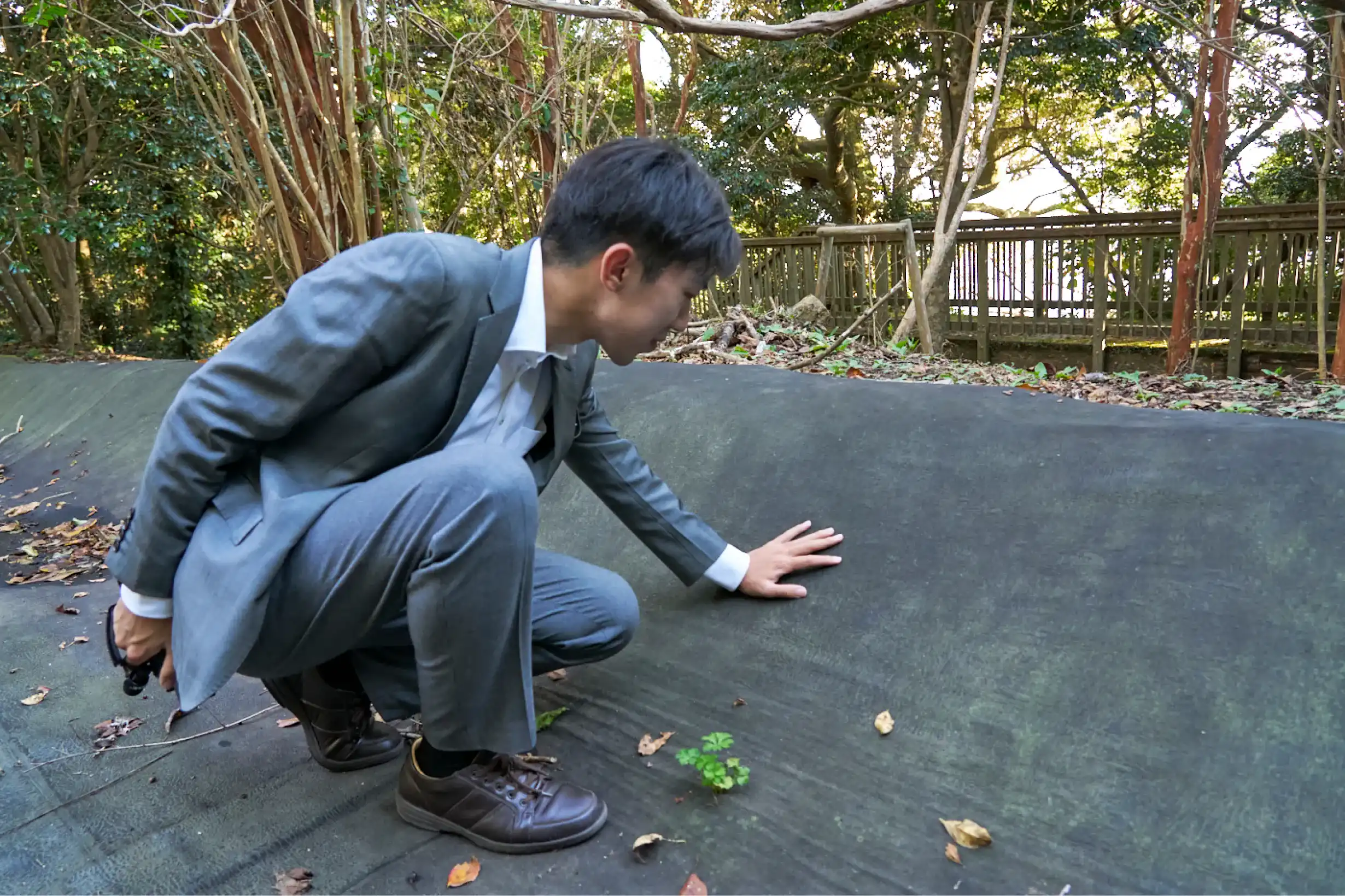 屈んで集水シート跡に触れるスーツさん