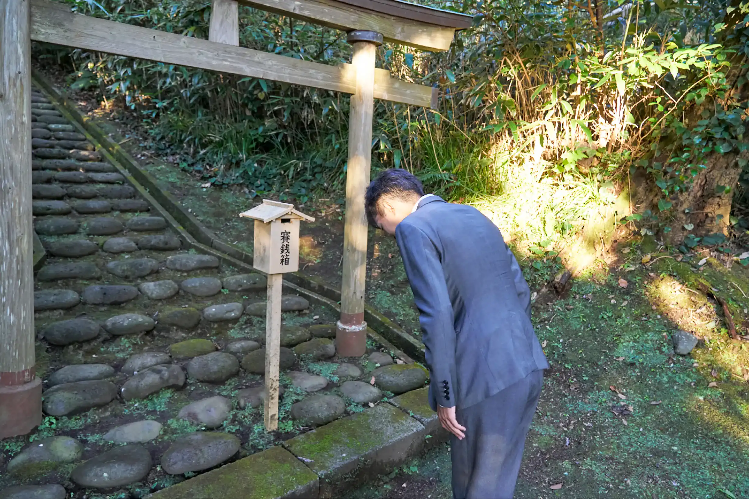 賽銭箱にお賽銭をして礼をするスーツさん