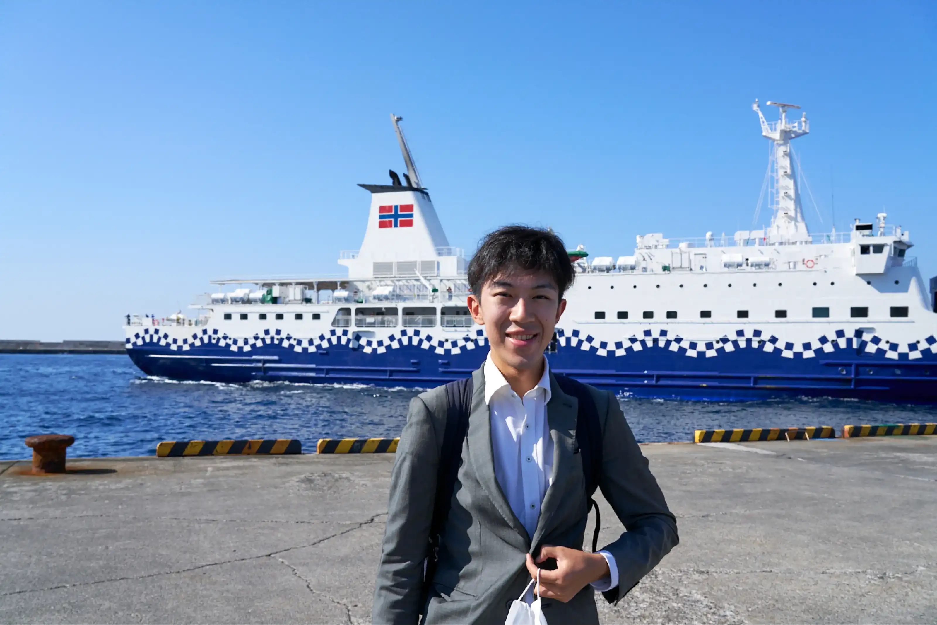 利島港で船をバックに笑顔のスーツさん
