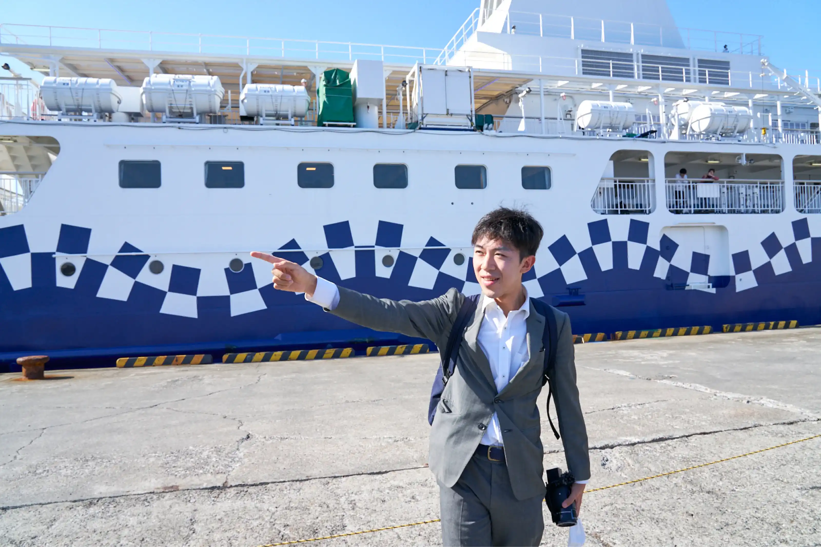 船の前で指差しポーズをするスーツさん